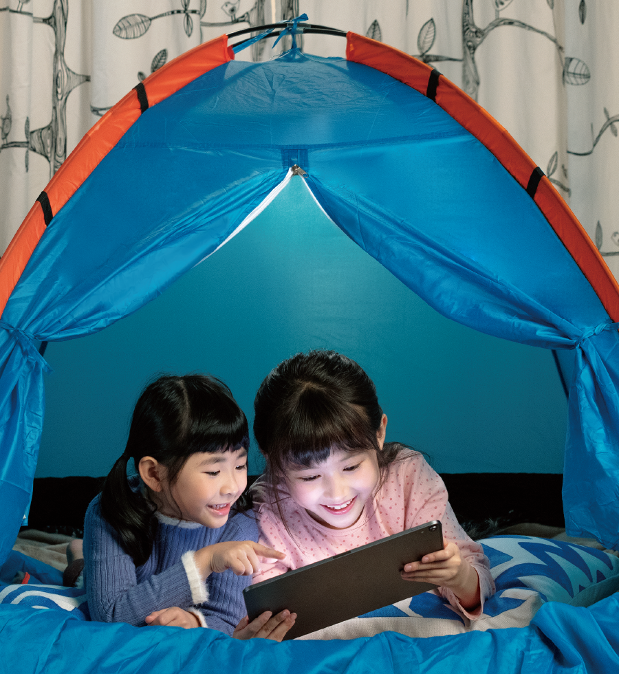 Sisters using tablet under the tent in their room